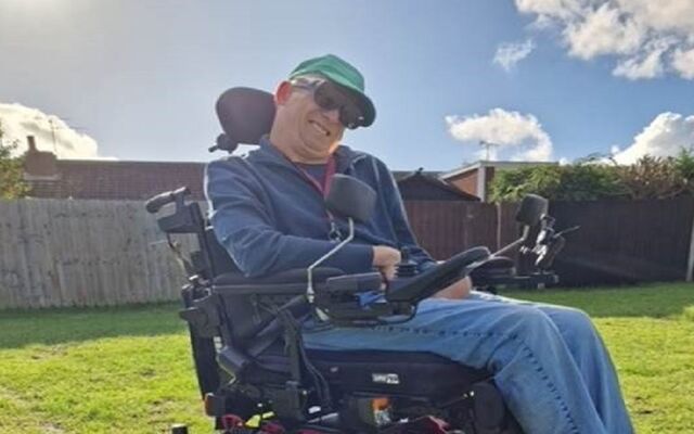 Glen smiling in wheelchair in garden sun shining