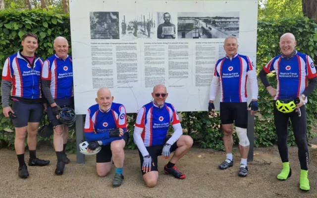 Cyclists in their Fund jerseys standing in front of museum board