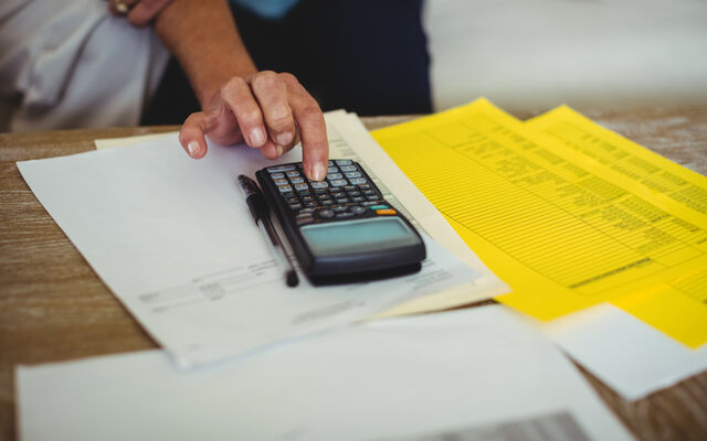 Person pressing calculator on table of paperwork