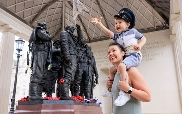 A child flying a tin foil aeroplane on his mum's shoulders outside the Bomber Command Memorial