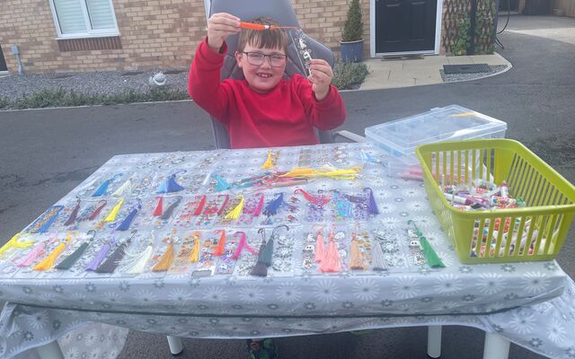 Logan outside home with table holding up his bookmarks