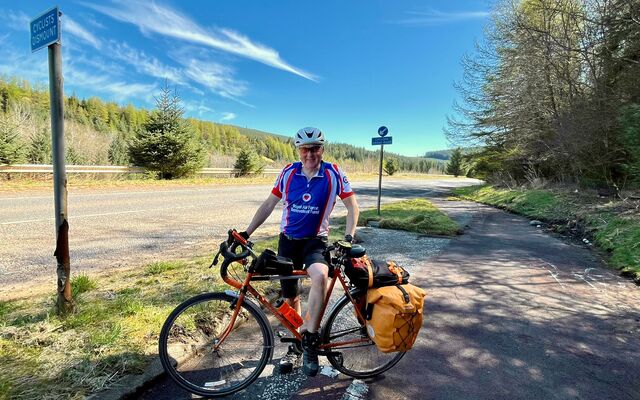 Tony wearing Fund vest standing with bike with blue skies and road behind him