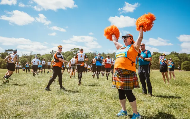 A lady with pom poms at a Tough Mudder event cheering on particpants.