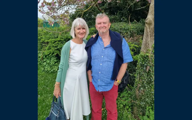 Allan and Caroline standing in front of greenery smiling