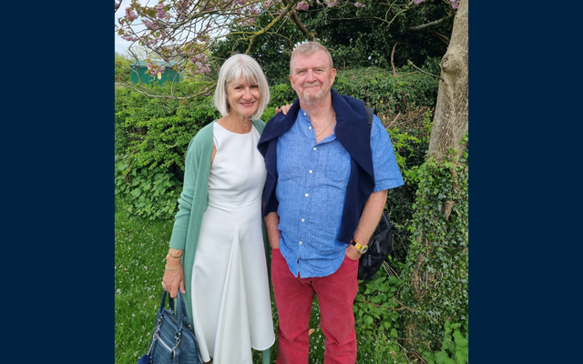 Allan and Caroline standing in front of greenery smiling