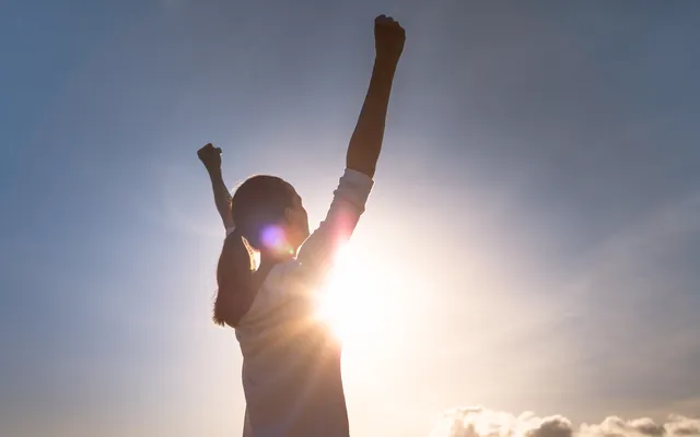 Woman with hands up as sun beams 