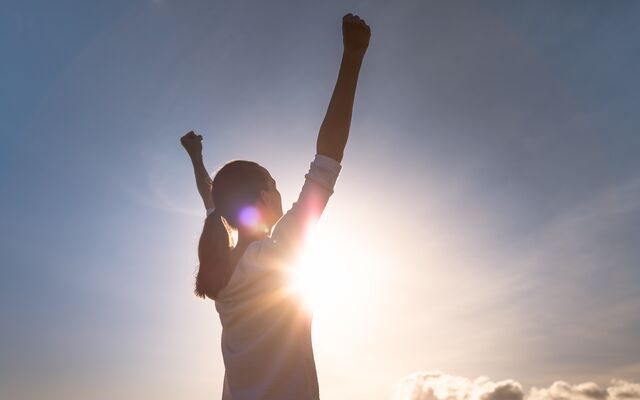 Woman with hands up as sun beams 