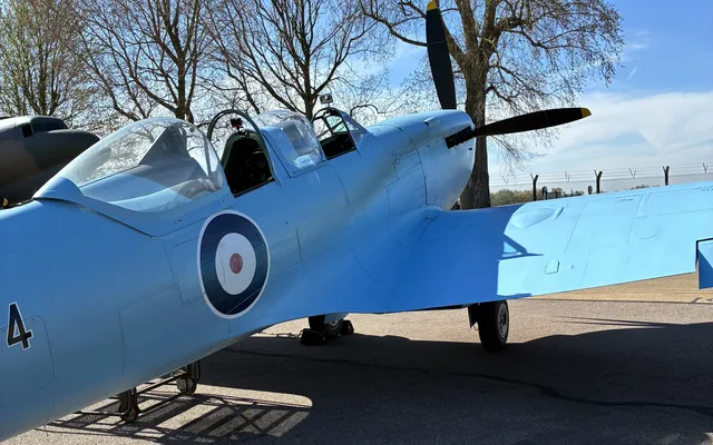 A blue Spitfire on the ground, from behind looking at the two, open cockpits
