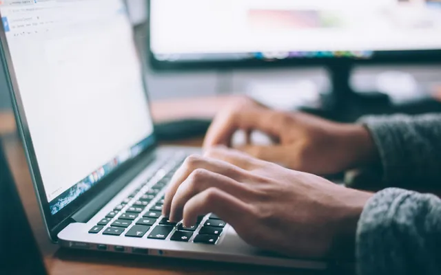 Close up image of a pair of hands typing at a laptop 