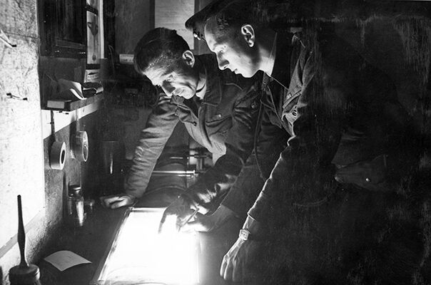 An RAF Flight Sergeant and Flying Officer analysing photographic reconnaissance prints at B8/Sommervieu, Normandy.