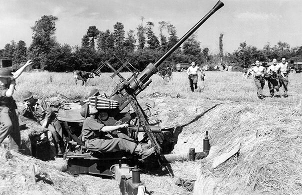 An RAF Regiment crew mans a 40mm Bofors anti-aircraft gun near an advanced landing ground in Normandy, as other personnel run to their posts during an alert.