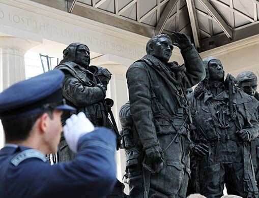 An RAF regiment serviceman salutes the Bomber Command Memorial statues.