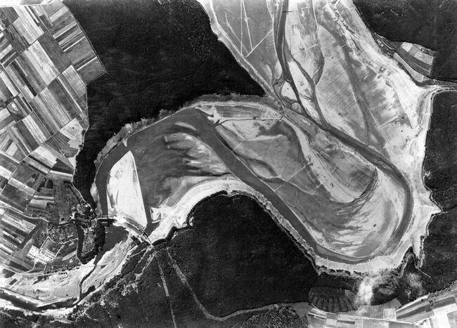 The Eder Dam, Germany, two months after the 'Dambusters' raid on 16/17 May 1943 by 617 Squadron. The reservoir (Edersee) is now completely dry and, on the river bed in front of the breached dam (top right) a light railweay has been construction in preparation for its repair. A new hutted encampment for workers has also been built to the right of the dam. Crown Copyright, MOD.