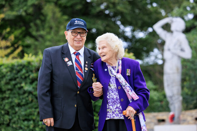 Reg and Sybil holding hands smiling in front of garden