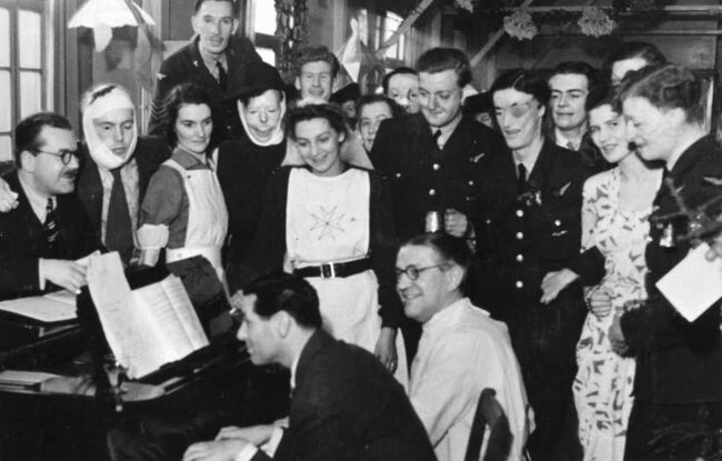 Black and white photo of GPC members around the piano singing