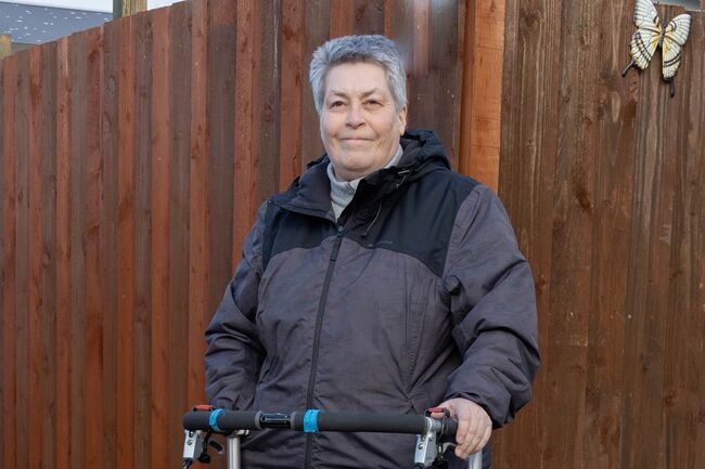 Yvonne standing with walker in front of brown fence