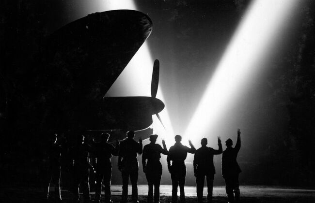 Ground crew of 514 Squadron at Waterbeach, Cambridgeshire, return the V-sign to a neighbouring searchlight as they celebrate VE Day, 8 May 1945.
