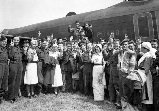 Ex-prisoners of war, along with attending nurses, give the "V for Victory" salute after being repatriated back to Dunsfold, Surrey, on board a Lancasterof 83 Squadron on VE Day, 8 May 1945.