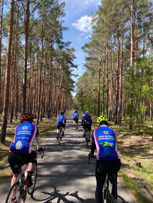 Cyclists on bikes with back to us cycling through tall trees wearing Fund jerseys