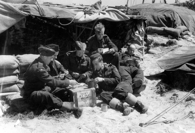 Members of 107 Beach Flight find time for a game of cards on a beach in Normandy, 22 June 1944. From left to right: Leading Aircraftsman G Harvey, Flight Sergeant JE Gould, Sergeant D Howells, LAC L Sexton and Corporals F Kirby and J Holland.
