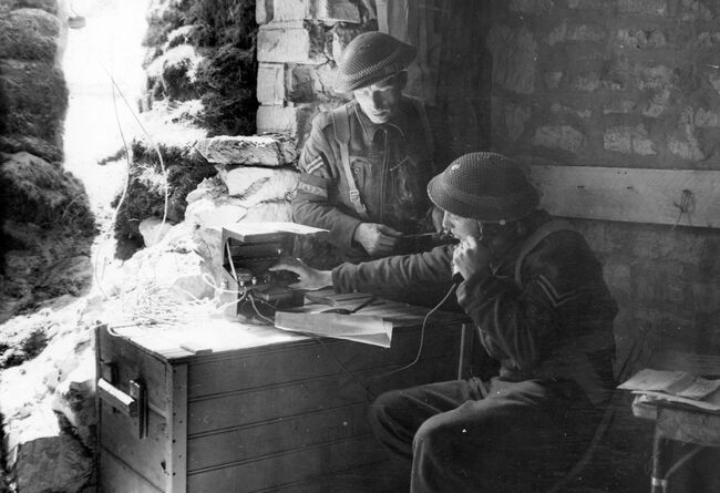 RAF Police of No 1 Beach Squadon in Normandy using a captured German dug-out as their headquarters, 24 June 1944. Although the area was regularly shelled by the Germans, being only 1.5 miles from the frontline. Standing is Corporal Norman Thorman from Manchester and Corporal Dan Deighton of Gateshead is using the field telephone.