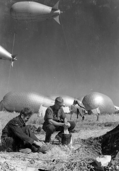 Two RAF servicing commandos take time to wash their laundry at an airfield in Normandy against a backdrop of barrage ballons, late June 1944.