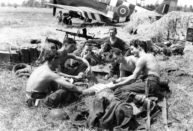 Leading Aircraftman George Langley, a servicing commando from Tewkesbury takes a break while armourers fit a 500lb bomb beneath the wing of a Mustang III of 122 Squadron at B7/Martragny, Normandy, on 25 June 1944.