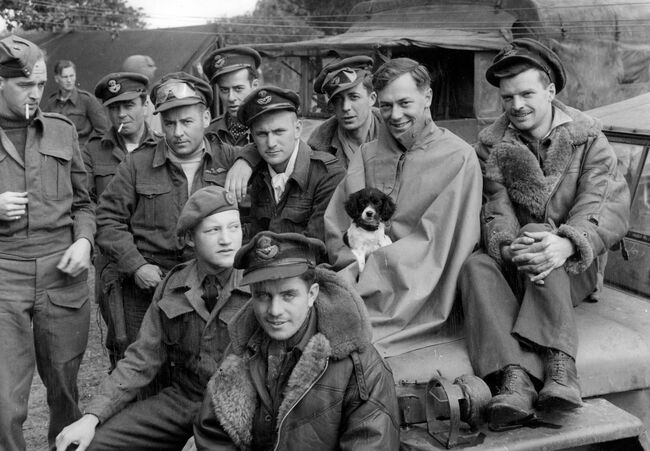 Pilots of 416 (City of Oshawa) Squadron RCAF await their next briefing at B2/Bazenville, 28 June 1944. One of the pilots is holding the squadron's mascot, "Type".