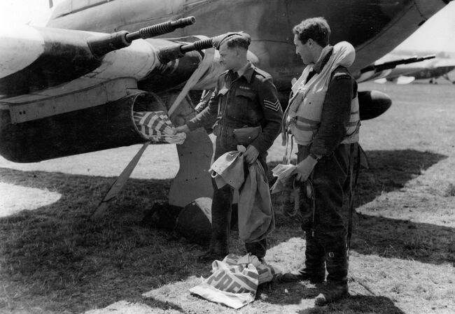 Sergeant H Stillwell unloads mail bags from the underwing tanks of a Hawker Hurricane IIC of 1697 (Air Despatch Delivery Service) Flight at Northolt, Middlesex, B2/Bazenville after a flight from B2/Bazenville in Normandy on 29 June 1944. The pilot, Flight Lieutenant WV Melbourne, looks on.