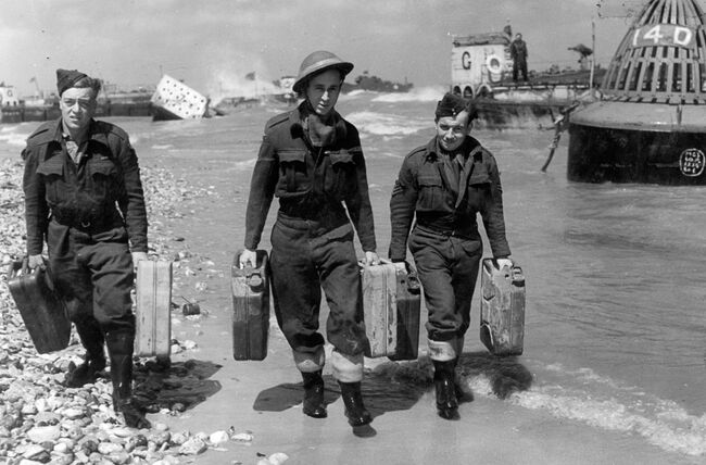 Leading Aircraftsmen G Harvey (left) and L Sexton, centre, with Flight Sergeant JE Gould, of 107 Beach Flight carrying jerricans of petrol along a beach in Normandy, 22 June 1944.