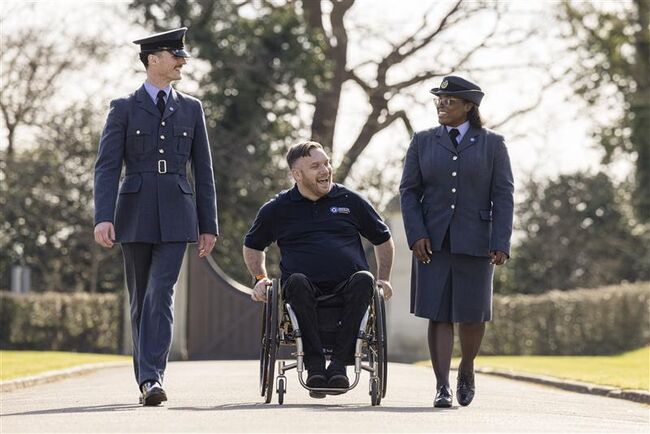 Image of a male and female serving RAF personnel with a veteran in a wheelchair walking and talking in an outdoor setting