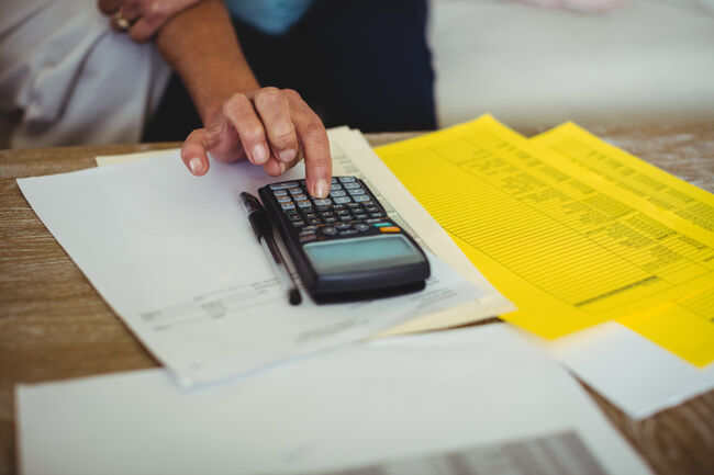 Person pressing calculator on table of paperwork