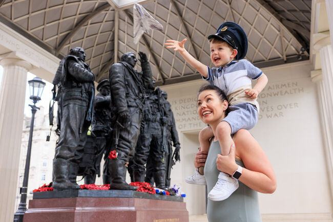 A child flying a tin foil aeroplane on his mum's shoulders outside the Bomber Command Memorial