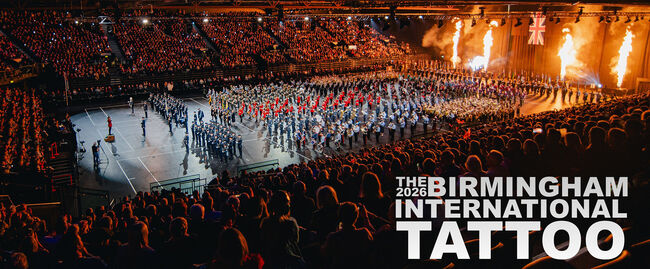 The Birmingham International Tattoo poster with an image of a band in an arena, with spectacular lights around the arena and flames.