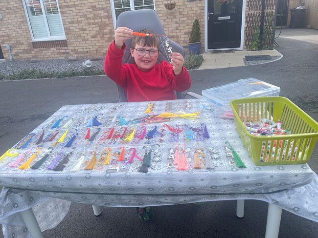 Logan outside home with table holding up his bookmarks