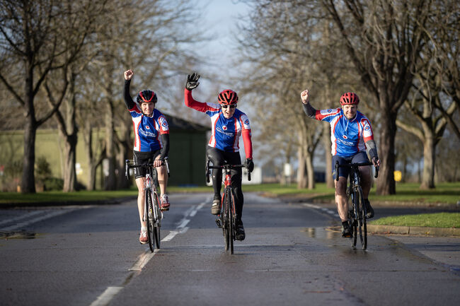 3 cyclists on their bikes with 1 arm raised 