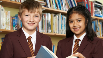 School children in their school uniform holding open a book and smiling.