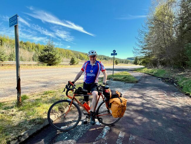 Tony wearing Fund vest standing with bike with blue skies and road behind him