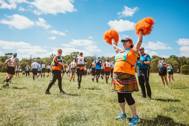 A lady with pom poms at a Tough Mudder event cheering on particpants.