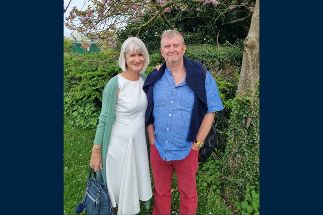 Allan and Caroline standing in front of greenery smiling