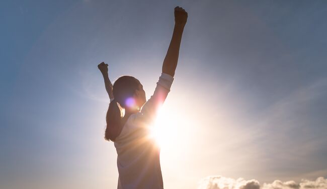 Woman with hands up as sun beams 
