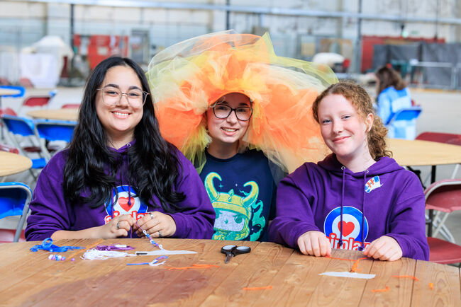 three Airplay attendees sat at craft table one with elaborate head dress on