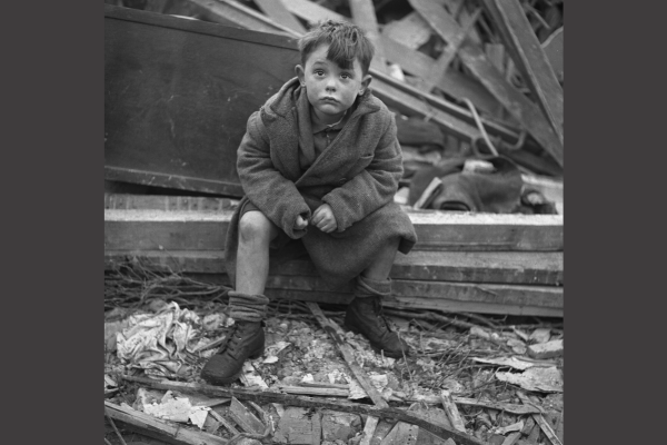 A black and white picture of a child sat on a step amongst broken buildings and rubble.